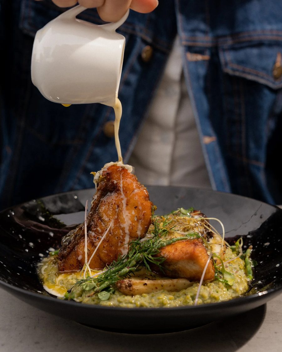 Pan-fried barramundi being finished with sauce
